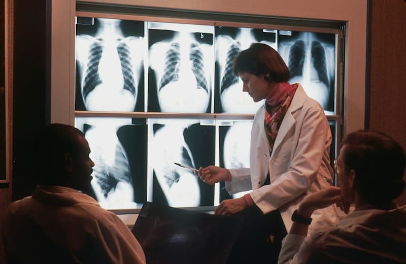 Médica explicando radiografías de tórax a su equipo en una sala de revisión